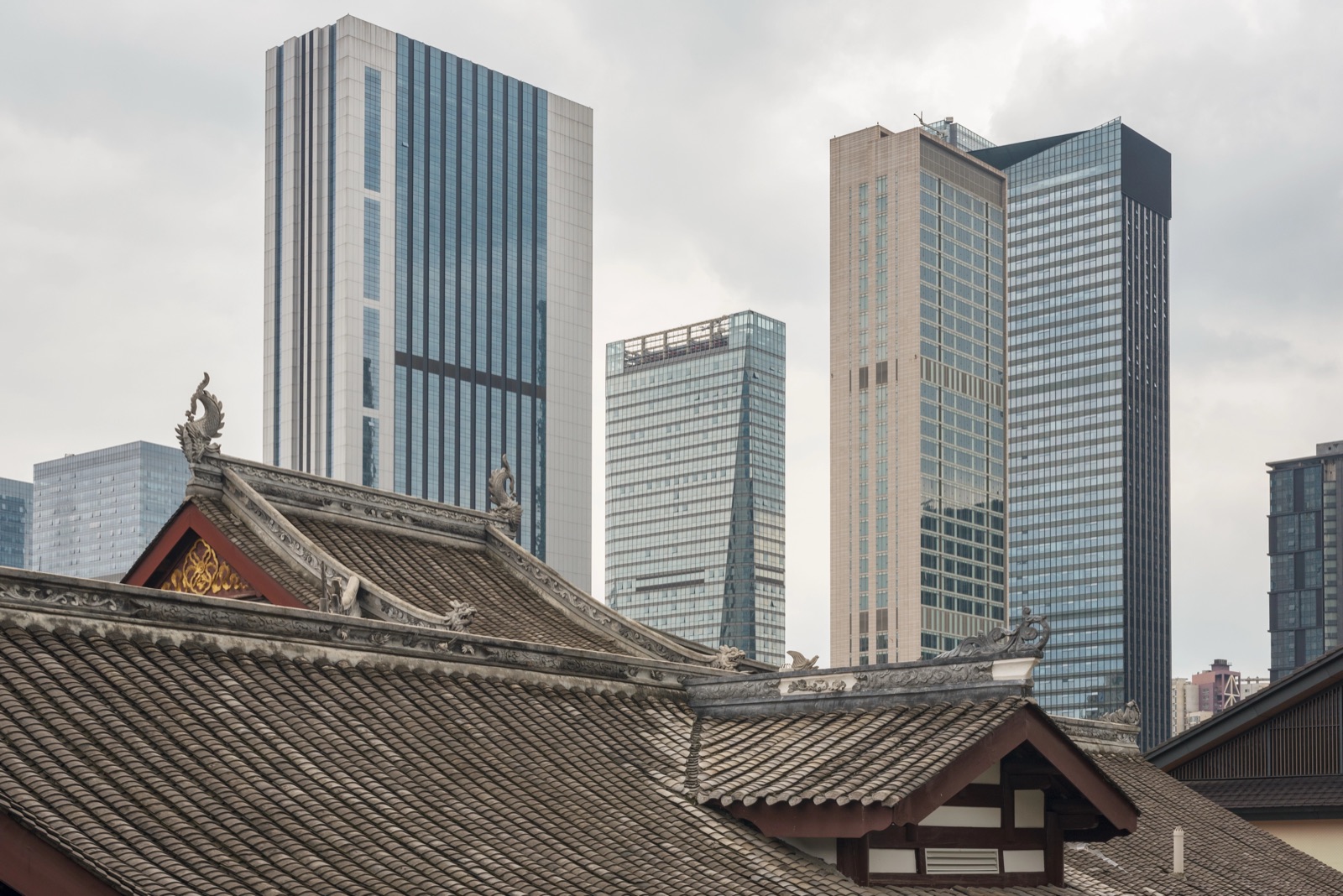 Curved tile rooftops of a traditional temple set against modern Chinese skyscrapers.